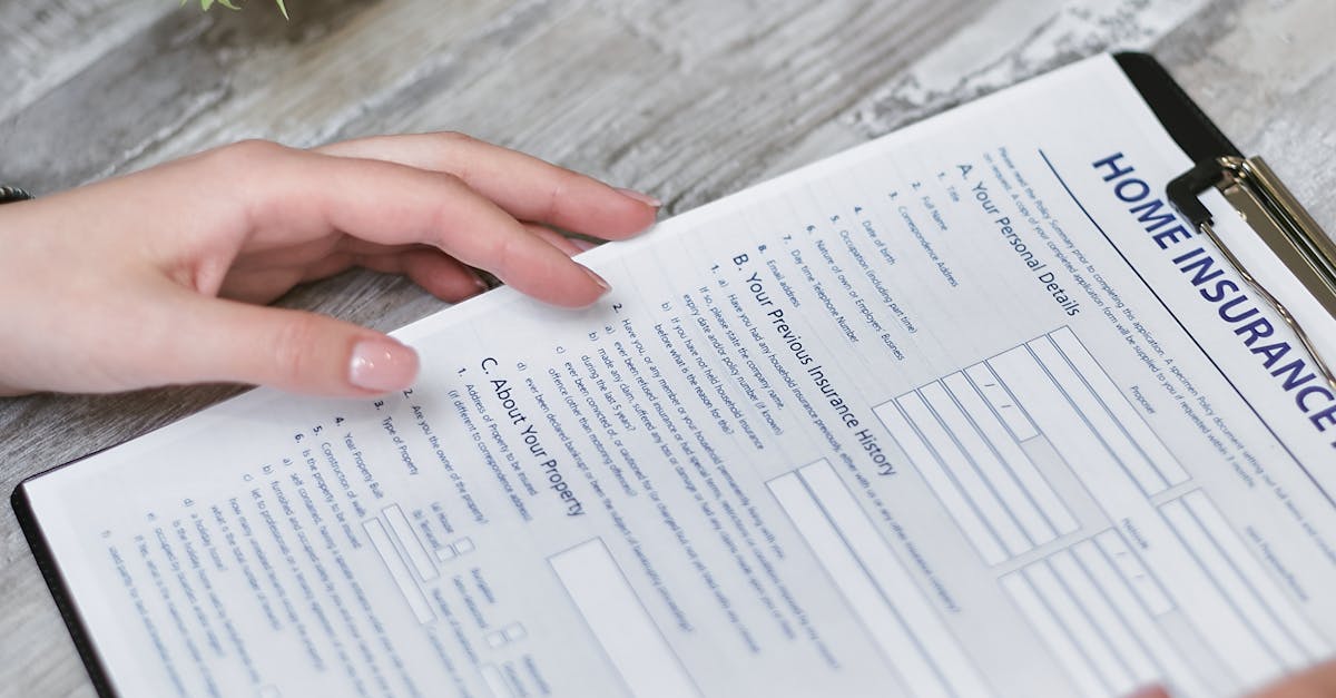 Close-up of hands holding a home insurance document indoors, showing personal details section.